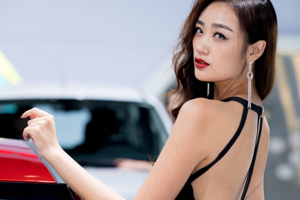 a-woman-in-a-black-dress-standing-next-to-a-red-car-qaltdhrq5xe